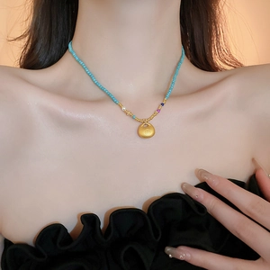 Détail d'un collier ras du cou perlé avec pendentif cadenas Fu doré porté par le mannequin