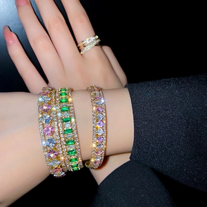Luxuriöse goldene Armreifen und Ringe mit rosa und grünen Zirkonia am Handgelenk
