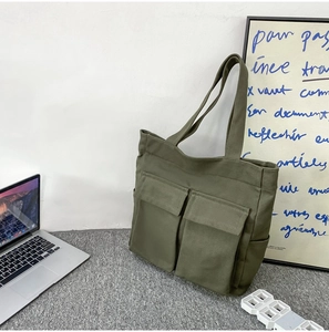 Olive green canvas tote bag with front pockets on a grey rug in an office setting