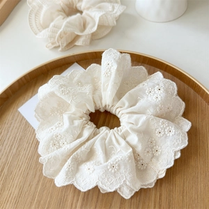 Détail d'un chouchou en dentelle crème avec broderie sur un plateau en bois