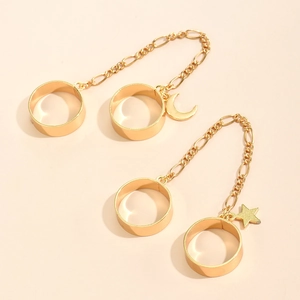 Detail of gold chain rings featuring star and crescent moon pendants on a beige background