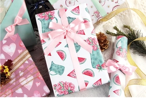 Close-up of pastel floral gift wrapping paper with pink and gold ribbons on white fabric