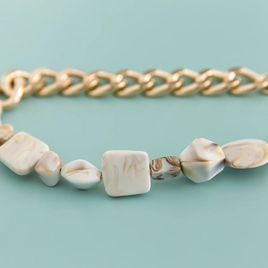 Close-up of golden metal chain with marble texture acrylic beads in mixed shapes