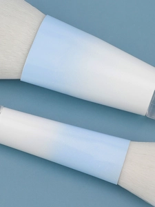 Macro detail of soft white synthetic bristles with light blue gradient metal ferrule