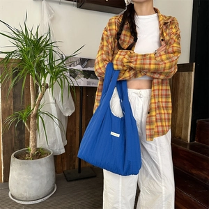 Detail of royal blue pleated fabric tote bag showing texture and white label on strap