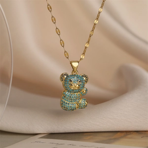 Detail of gold necklace with blue pave bear pendant hanging on soft beige fabric