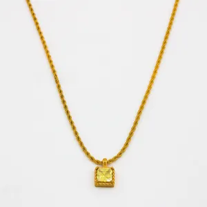 Gros plan d'un collier chaîne torsadée dorée avec pendentif carré en pierre jaune