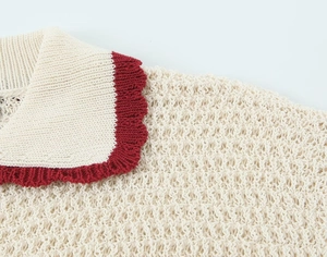 Detail shot of white knit polo top featuring red wavy trim and hollow texture details