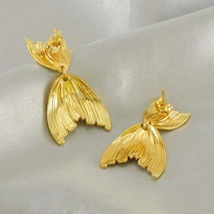 Macro shot of gold fishtail earrings with striped texture on silver silk background