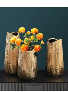 Macro detail of electroplated gold ceramic vases with textured finish and orange faux flowers