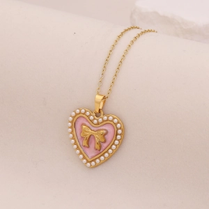 Vintage gold necklace with pink enamel heart pendant, gold bow, and pearl border detailing