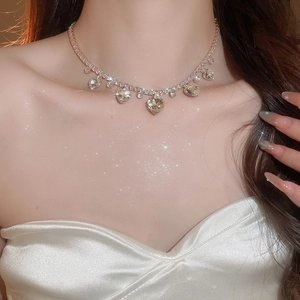 Close-up of golden heart crystal tassel necklace worn on neck in elegant lighting