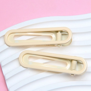 Detail view of two cream beige glossy metal hair clips on a wavy pink surface