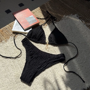 Detail of black bikini with textured fabric featuring golden ring and pearl charms