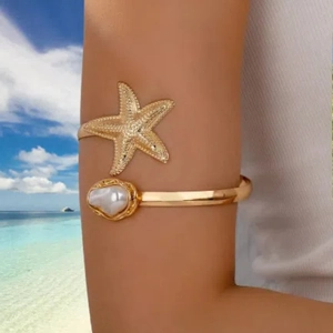 Gold starfish arm cuff with faux pearl on a model with a scenic ocean beach background