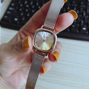 Close-up of rose gold square quartz watch with mesh strap worn in an office setting