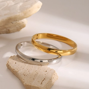 Dettaglio di bracciali rigidi in acciaio inossidabile oro e argento su pietra