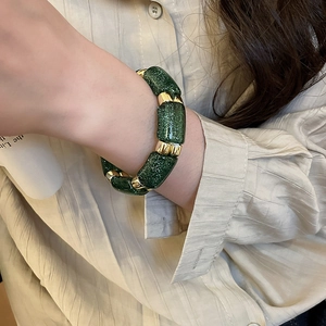 Close-up of green acrylic bracelet with gold metal clasp on a model's wrist