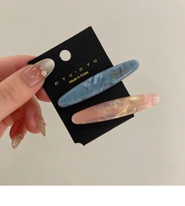 Détail de deux barrettes en acétate bleu Morandi et rose orangé avec texture marbrée
