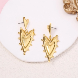 French vintage gold heart-shaped dangle earrings on a white stand with pink background