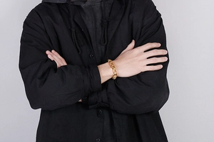 Detail of a vintage gold skull chain bracelet worn by a male model over black attire