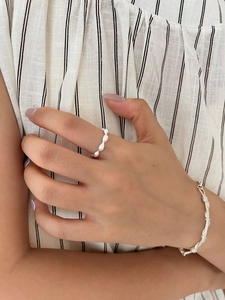 Close-up of minimalist textured sterling silver ring and woven bangle on hand