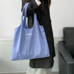 Blue canvas tote bag with Simplicity print shown on model for capacity and style
