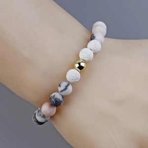 Pink Zebra Jasper and gold bead bracelet with natural volcanic stone on a display stand