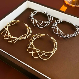Detailed view of woven hollow C-shape earrings in gold and silver finish on tray