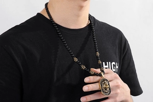 Detail of lion head relief pendant on black beaded chain necklace worn by a model