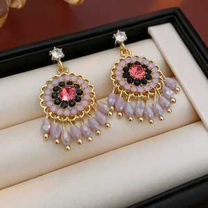Macro shot of gold floral earrings with pink crystals and purple tassel droplets