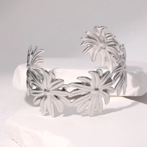 Silver daisy floral cutout bangle in polished stainless steel on white stone background