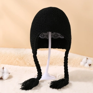 Detail of black knit winter baby hat featuring braided ear flaps and soft tassel ends
