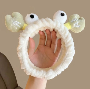 Close-up of a plush white crab-shaped headband with big eyes and green pincers