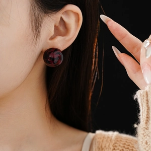 Close-up of model wearing round dark red leopard print resin stud earrings on black background