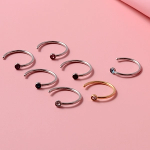 Flat lay of seven C-shaped stainless steel nose rings with colorful inset gemstones
