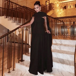 Elegant black off-shoulder maxi evening dress with a cape detail on a luxury staircase