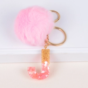 Close-up of fluffy pink pompom and golden glitter resin letter J keychain accessory