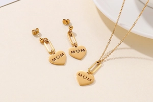 Detail of gold MOM heart pendant necklace and earrings set on a minimalist tray