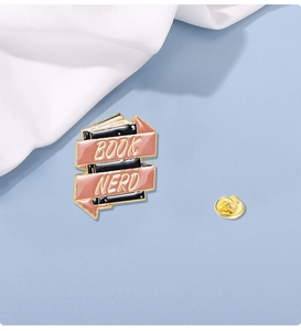 Detail of enamel book brooch with pink ribbon and Book Nerd text on blue background