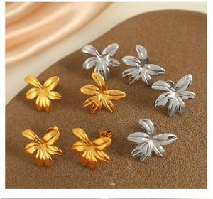 Detailed view of floral stud earrings in gold and silver finishes on a brown surface
