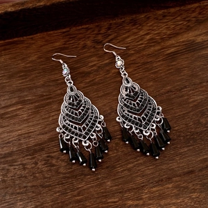 Close-up of vintage heart tassel earrings with black rhinestones on a wooden base