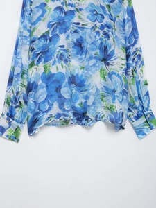 Detail of blue floral print shirt featuring vibrant green leaves and buttoned cuffs