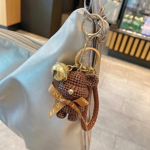 Handmade brown crochet bear keychain with gold bell and ribbon on a leather handbag