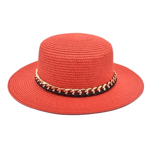 Détail d'un chapeau de paille rouge à toit plat avec chaîne dorée et ruban tressé noir