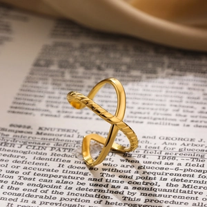 Polished 18K gold-plated twisted cross open ring shown on an artistic book background