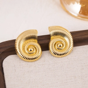 Exaggerated golden conch earrings on dark wood tray with linen mat for elegant jewelry display