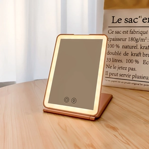 Detail of rose gold foldable LED travel mirror with touch controls on wood surface