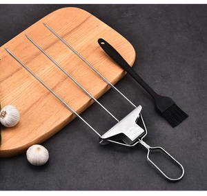 Three-prong stainless steel BBQ fork and black silicone brush on dark slate surface