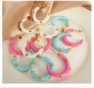 Close-up of colorful enamel C-shape heart earrings in gold finish on silk background
